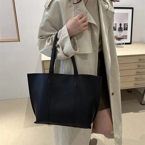 Minimalist black matte leather tote bag shown in a professional lifestyle fashion setting