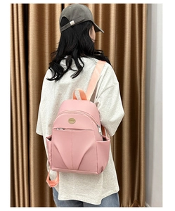 Rear view of model wearing a pink water-resistant nylon backpack with multi-pocket design