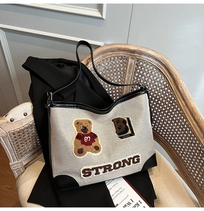 Detail view of canvas tote bag featuring embroidered bear patch and black leather trim