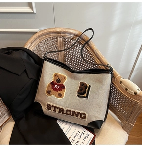 Close-up of canvas tote bag featuring embroidered bear patches and strong lettering