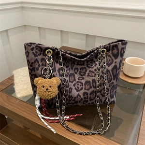 Sac fourre-tout à imprimé léopard avec chaîne dorée et pendentif ours sur une table