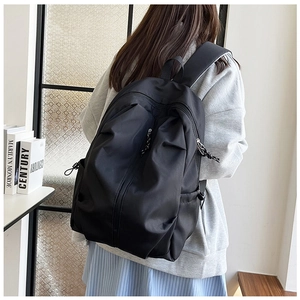 Close-up of black nylon backpack on model showing side pocket and woven zipper pull detail