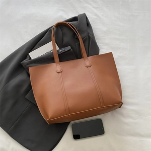 Detailed view of brown faux leather tote bag with vertical stitching and slim straps
