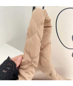Dettaglio della tracolla imbottita trapuntata di una borsa tote beige in nylon lucido
