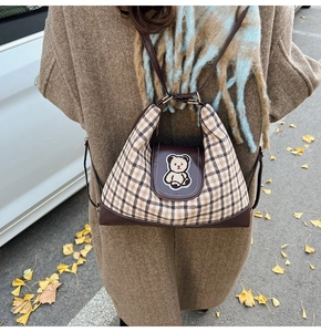 Detail of a brown plaid tote bag featuring a cute bear patch and leather trim detail