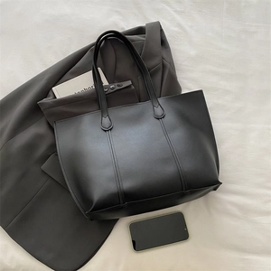 Close-up of a large black faux leather tote bag with office accessories on a flat surface