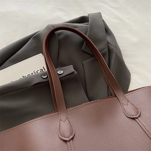 Close-up of brown leather tote bag with reinforced handles and teardrop stitching detail
