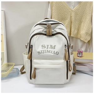 Close-up of a white nylon backpack with SJM logo detail in a cozy student setting