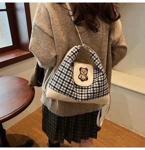 Detail view of plaid crossbody bag featuring a cute bear patch worn by a model