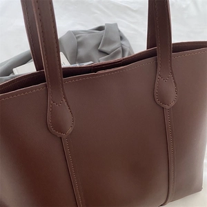Close-up of brown faux leather tote bag showing double stitching and top handle details