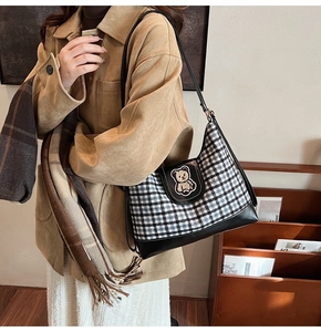 Detail of checkered canvas shoulder bag featuring a cute brown bear embroidery and leather trim