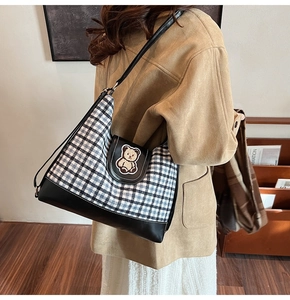 Detail view of canvas tote bag with teddy bear patch and checkered pattern held by model