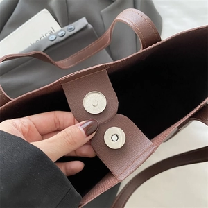 Close-up of dark brown tote bag showing dual magnetic snap closures and pebbled leather texture