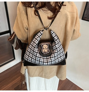 Detail of checkered canvas tote bag with plush bear patch and leather bottom trim