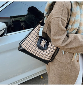 Detail of vintage canvas tote with brown plaid fabric, leather base and bear patch