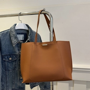 Detail view of a brown faux leather tote bag hanging next to a denim jacket in a studio