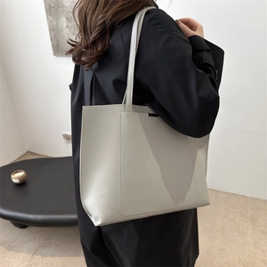 Minimalist beige tote bag shown on model wearing a dark coat in a home setting