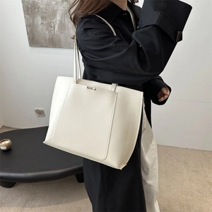 Model wearing a large cream tote bag showing the minimalist PU leather and slim shoulder strap
