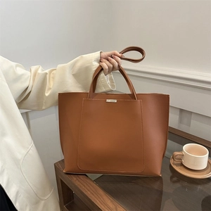 Detail of a dark brown leather tote bag with a minimalist front pocket and metal trim