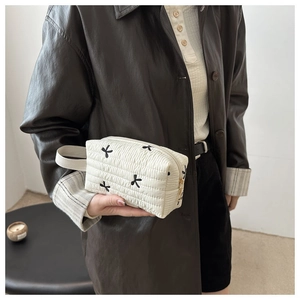 Détail de la trousse matelassée blanche avec nœuds brodés noirs et fermeture dorée