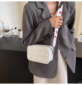 Détail du sac bandoulière blanc matelassé en cœurs avec broderie de cœurs rouges sur la sangle