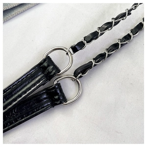 Détail d'une bandoulière en similicuir noir brillant tressé avec une chaîne en métal argenté