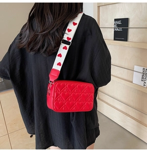 Détail du sac bandoulière rouge matelassé avec large sangle à motifs pour femmes