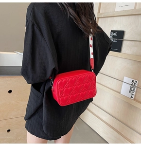 Détail du sac à bandoulière rouge matelassé avec une sangle large à motifs