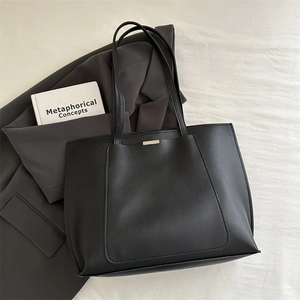 Flat lay of black large capacity tote bag with golden metal detail on textured fabric
