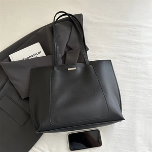 Close-up of black leather tote bag with gold metal trim on elegant white fabric