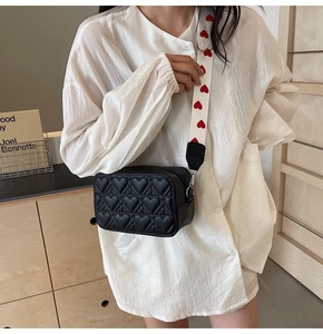 Détail du sac bandoulière noir matelassé cœur avec large bandoulière à motifs blancs