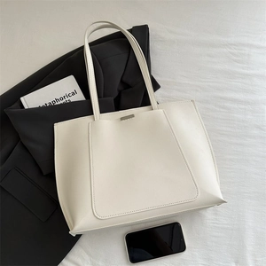Detail view of white leather tote bag with large front pocket and silver metal bar accent