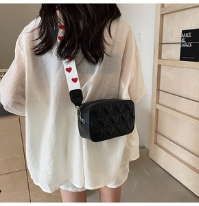 Détail du sac bandoulière noir matelassé avec motif cœur et large sangle tissée