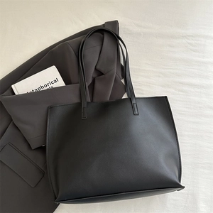 Flat lay of minimalist black large tote bag with slender straps on grey blazer and book