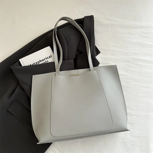 Detailed macro view of the light gray tote bag featuring slim straps and metal logo bar