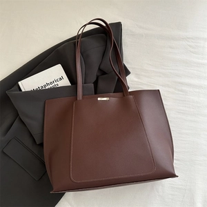 Detail of dark brown tote bag with gold metal hardware on light textured fabric