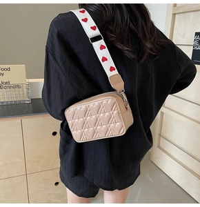 Détail du sac à bandoulière matelassé beige avec large sangle décorative à cœurs rouges