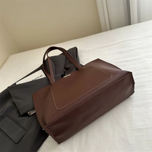 Close-up of a large dark brown tote bag with decorative stitching on white bedding