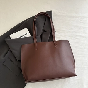 Detail view of large dark brown leather tote bag on casual blazer for office commute