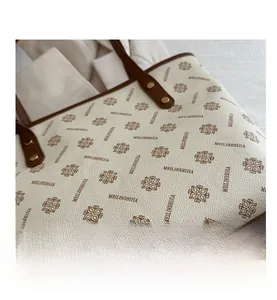Detail of white tote bag featuring floral monogram pattern and brown leather handles