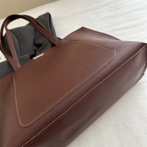 Detail of deep brown leather tote bag showing fine texture and metallic logo plaque