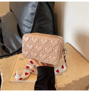 Détail du sac beige matelassé cœur avec bandoulière à motifs cœurs sur socle en pierre