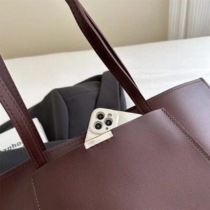 Detail view of burgundy tote bag showing front pocket with leather lychee grain texture
