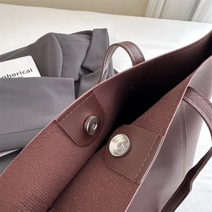 Detail of silver magnetic closure and fine stitching on a dark brown leather tote bag