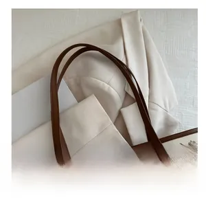 Detail of a brown leather shoulder strap with metal rivet on a cream tote bag