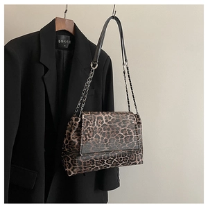 Détail du sac à bandoulière léopard avec chaîne argentée porté sur une veste de blazer noire