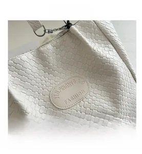 Detail shot of white woven leather texture with an oval brand patch on a tote bag