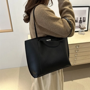 Classic minimalist large capacity black leather tote bag worn as a shoulder bag
