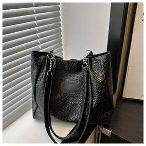 Detail of black woven tote bag featuring silver chain strap and refined leather texture