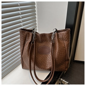 Detailed view of dark brown woven texture tote bag with leather logo patch and silver chain strap